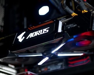A close-up view of a high-performance graphics card inside a computer, featuring prominent branding and illuminated components. The cables and surrounding hardware components are partially visible, contributing to a sleek, modern tech aesthetic.